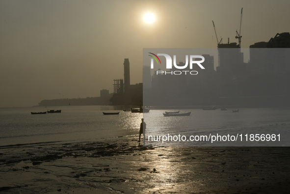 A man walks on a beach with a backdrop of a cityscape in Mumbai, India, on December 11, 2024. 