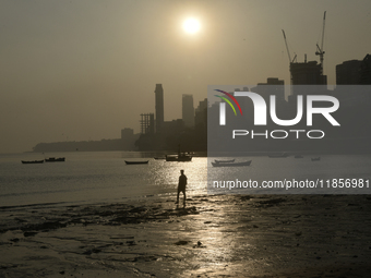 A man walks on a beach with a backdrop of a cityscape in Mumbai, India, on December 11, 2024. (