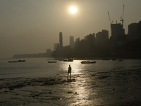 A man walks on a beach with a backdrop of a cityscape in Mumbai, India, on December 11, 2024. (