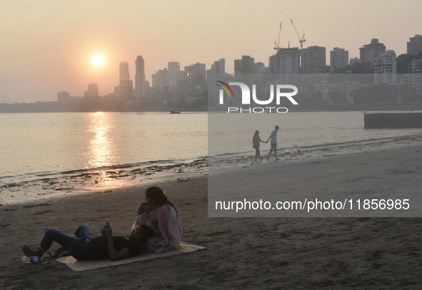 Couples are seen at a sea beach with a backdrop of a cityscape in Mumbai, India, on December 11, 2024. 