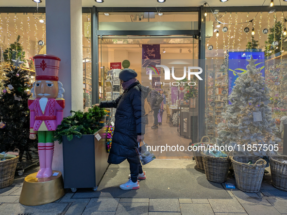 A woman picks up some Christmas greenery outside a decorated store in Munich, Bavaria, on December 11, 2024. The window displays feature spa...