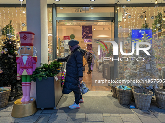 A woman picks up some Christmas greenery outside a decorated store in Munich, Bavaria, on December 11, 2024. The window displays feature spa...