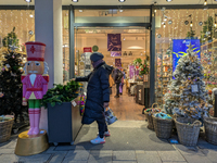 A woman picks up some Christmas greenery outside a decorated store in Munich, Bavaria, on December 11, 2024. The window displays feature spa...