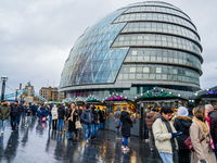 Visitors enjoy the festive atmosphere at the Christmas market near City Hall, with Tower Bridge in the background, in London, United Kingdom...