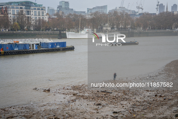 A lone individual walks along the muddy Thames shoreline during low tide as Storm Darragh brings overcast skies and rain on December 7, 2024...