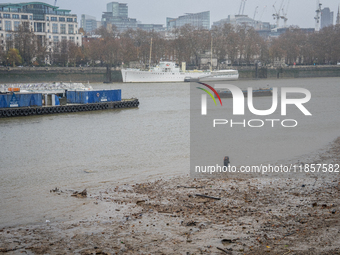 A lone individual walks along the muddy Thames shoreline during low tide as Storm Darragh brings overcast skies and rain on December 7, 2024...