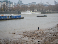 A lone individual walks along the muddy Thames shoreline during low tide as Storm Darragh brings overcast skies and rain on December 7, 2024...