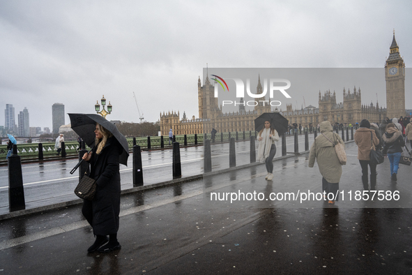 Pedestrians with umbrellas cross Westminster Bridge in front of the Houses of Parliament during Storm Darragh on December 7, 2024, in London...