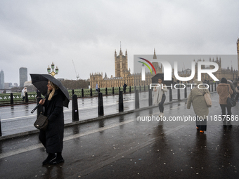 Pedestrians with umbrellas cross Westminster Bridge in front of the Houses of Parliament during Storm Darragh on December 7, 2024, in London...