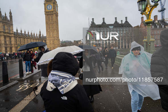 People wearing raincoats and carrying umbrellas cross Westminster Bridge near Big Ben during Storm Darragh on December 7, 2024, in London, U...