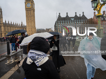 People wearing raincoats and carrying umbrellas cross Westminster Bridge near Big Ben during Storm Darragh on December 7, 2024, in London, U...