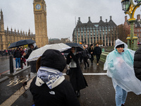 People wearing raincoats and carrying umbrellas cross Westminster Bridge near Big Ben during Storm Darragh on December 7, 2024, in London, U...