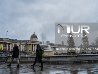 People walk past the fountains at Trafalgar Square under cloudy skies during Storm Darragh on December 8, 2024, in London, United Kingdom. L...