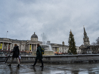 People walk past the fountains at Trafalgar Square under cloudy skies during Storm Darragh on December 8, 2024, in London, United Kingdom. L...