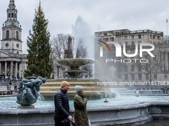 People walk past the fountains at Trafalgar Square under cloudy skies during Storm Darragh on December 8, 2024, in London, United Kingdom. L...