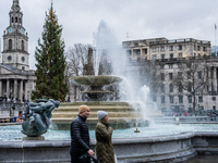 People walk past the fountains at Trafalgar Square under cloudy skies during Storm Darragh on December 8, 2024, in London, United Kingdom. L...