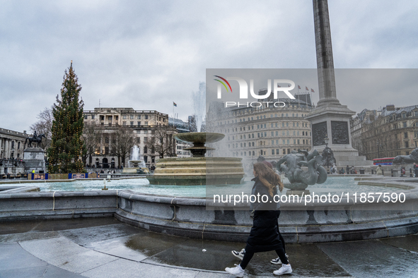 A woman walks past the fountains at Trafalgar Square under cloudy skies during Storm Darragh on December 8, 2024, in London, United Kingdom....