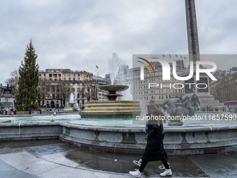 A woman walks past the fountains at Trafalgar Square under cloudy skies during Storm Darragh on December 8, 2024, in London, United Kingdom....