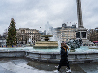 A woman walks past the fountains at Trafalgar Square under cloudy skies during Storm Darragh on December 8, 2024, in London, United Kingdom....