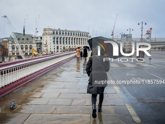 A woman holds an umbrella while walking across a wet bridge during Storm Darragh on December 8, 2024, in London, United Kingdom. London's Ro...