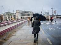 A woman holds an umbrella while walking across a wet bridge during Storm Darragh on December 8, 2024, in London, United Kingdom. London's Ro...