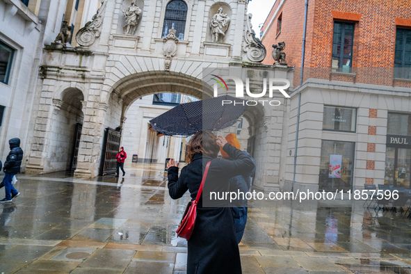 A woman struggles with her umbrella in gusty winds near a historic archway during Storm Darragh on December 8, 2024, in London, United Kingd...