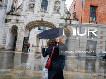 A woman struggles with her umbrella in gusty winds near a historic archway during Storm Darragh on December 8, 2024, in London, United Kingd...