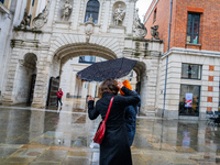 A woman struggles with her umbrella in gusty winds near a historic archway during Storm Darragh on December 8, 2024, in London, United Kingd...