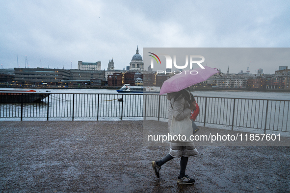 A woman with a pink umbrella walks along the riverbank with St. Paul's Cathedral in the background during Storm Darragh on December 8, 2024,...