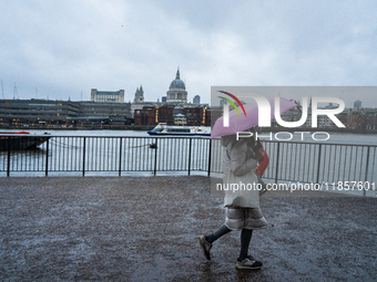 A woman with a pink umbrella walks along the riverbank with St. Paul's Cathedral in the background during Storm Darragh on December 8, 2024,...