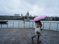 A woman with a pink umbrella walks along the riverbank with St. Paul's Cathedral in the background during Storm Darragh on December 8, 2024,...