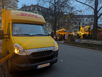 A yellow DHL delivery van parks near the Haidhauser Christmas Market in Munich, Bavaria, Germany, on December 11, 2024. The glowing lights o...