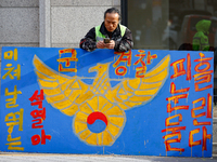 A protester leans against a hand-painted sign in front of the People Power Party's central headquarters in Yeouido, Seoul, South Korea, on D...