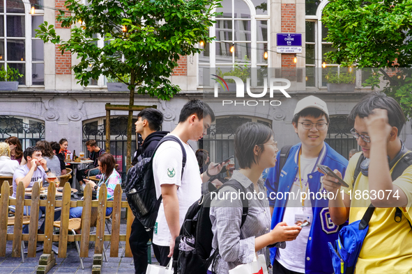 A group of Asian tourists gathers to check their smartphones, searching for directions while exploring the streets in Brussels, Belgium, on...