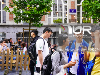 A group of Asian tourists gathers to check their smartphones, searching for directions while exploring the streets in Brussels, Belgium, on...