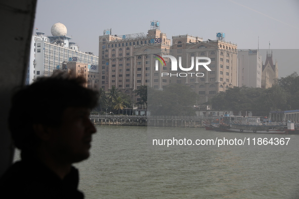 A man travels on a ferry in the waters of the Ganges River while the State Bank of India (SBI) regional office building is pictured in Kolka...