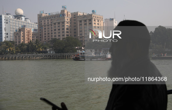 A man travels on a ferry in the waters of the Ganges River while the State Bank of India (SBI) regional office building is pictured in Kolka...