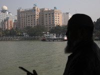 A man travels on a ferry in the waters of the Ganges River while the State Bank of India (SBI) regional office building is pictured in Kolka...