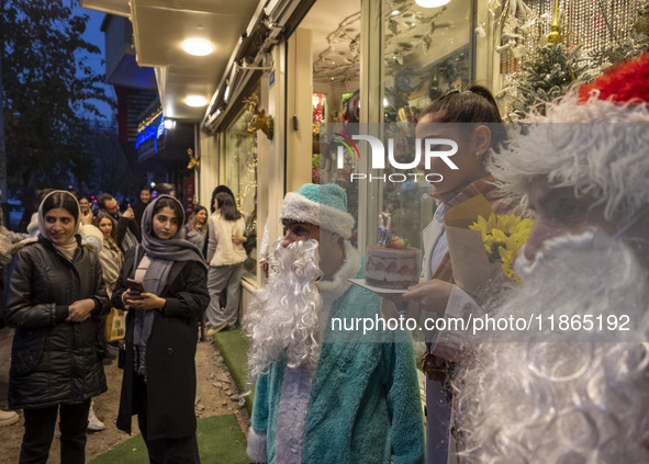 A young Iranian woman holds her birthday cake while standing next to two Iranian-Christian men dressed as Santa Claus during Christmas shopp...