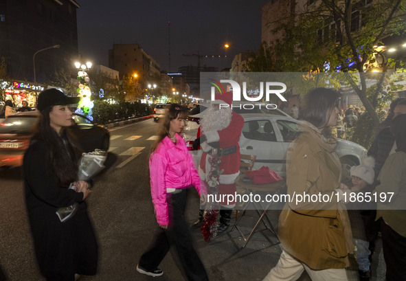 Young Iranian women walk past an Iranian-Christian man dressed as Santa Claus standing on a street-side during Christmas shopping in downtow...