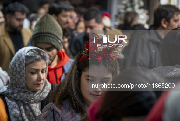 A young Iranian woman wears a Christmas accessory as she walks along a sidewalk while Christmas shopping in downtown Tehran, Iran, on Decemb...