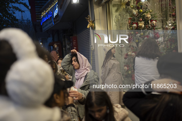 A young Iranian woman wearing a hat looks at a shop window decorated for Christmas shopping in downtown Tehran, Iran, on December 13, 2024....