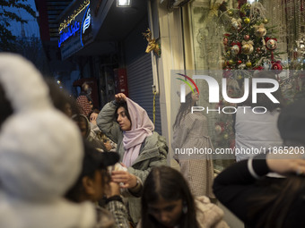 A young Iranian woman wearing a hat looks at a shop window decorated for Christmas shopping in downtown Tehran, Iran, on December 13, 2024....