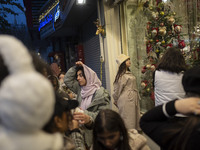 A young Iranian woman wearing a hat looks at a shop window decorated for Christmas shopping in downtown Tehran, Iran, on December 13, 2024....