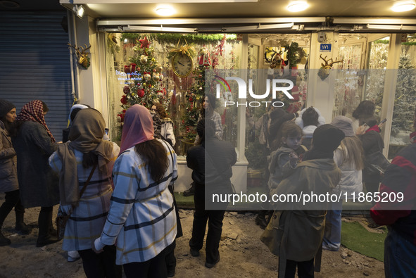 Young Iranian women stand on a sidewalk outside a shop decorated for Christmas shopping in downtown Tehran, Iran, on December 13, 2024. Whil...