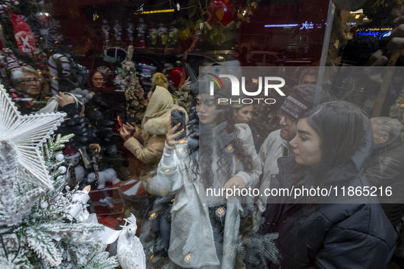 A young Iranian woman wearing a hat takes photographs of a shop window decorated for Christmas shopping in downtown Tehran, Iran, on Decembe...