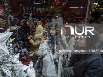 A young Iranian woman wearing a hat takes photographs of a shop window decorated for Christmas shopping in downtown Tehran, Iran, on Decembe...