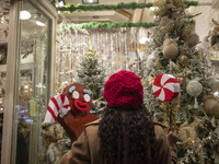 A young Iranian woman poses for a photograph in front of a shop window decorated for Christmas shopping while holding Christmas accessories...