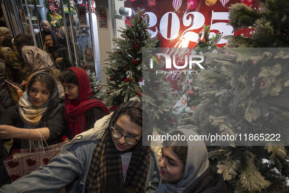 Young Iranian women stand together in front of Christmas trees that are placed outside a shop decorated for Christmas shopping in downtown T...