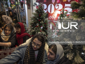 Young Iranian women stand together in front of Christmas trees that are placed outside a shop decorated for Christmas shopping in downtown T...